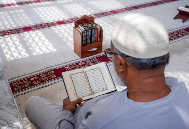 An old man sits quietly inside a mosque, reading the Quran